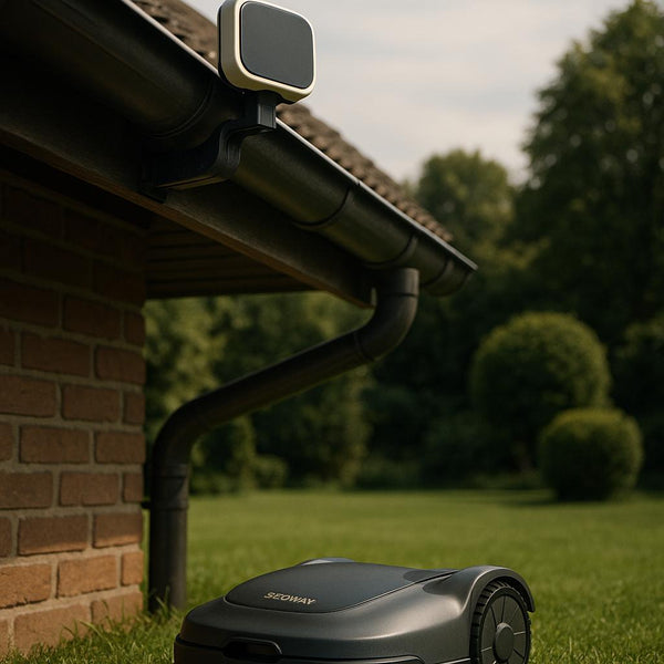 Robotplæneklipper ved siden af et hus med tagrender og grøn have i baggrunden.